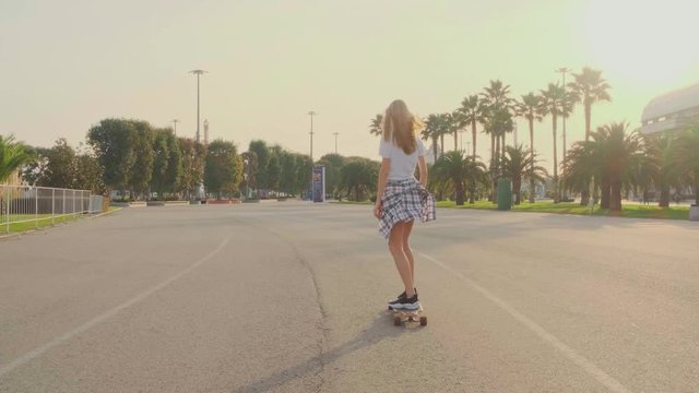 A girl in a white t-shirt and a plaid shirt on the belt rides a skateboard in the Park. Stylish woman rides a longboard fast through the open space in the Park, 60 fps.