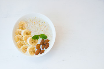 Oatmeal porridge with honey, banana and nuts in a plate on a white background on a white background. Top view.