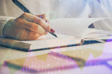 Double exposure of woman's hands making notes with forex graph hologram. Concept stock market...