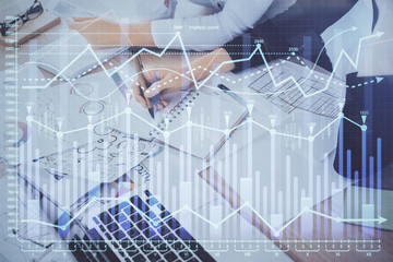 A woman hands writing information about stock market in notepad. Forex chart holograms in front. Concept of research. Double exposure