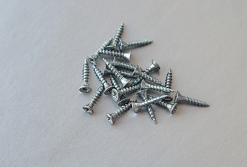 A pile of silver metal screws on a gray background. Selective focus.The view from the top