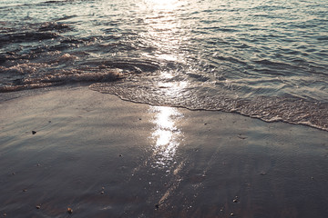 Black sand with sea wave ripple on the beach, sunset light reflection. Water and sand mix with mineral ore and Crude oil