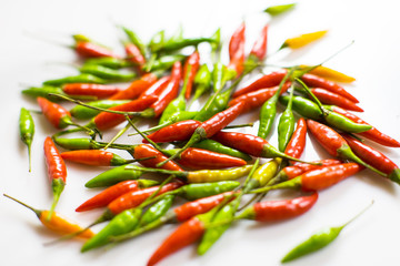 Many orange, green and red chilli peppers on white background with bokeh.