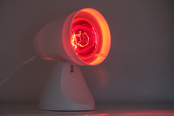 Infrared lamp glowing in the dark with its warming red light to cure for example colds or tensions.