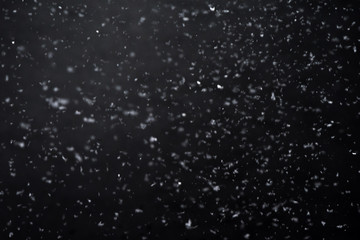 Falling  snow at night. Bokeh lights on black background, flying snowflakes in the air. Overlay texture. Snowstorm