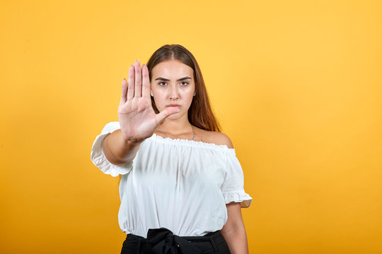 Serious young woman doing stop, pouse gesture isolated on orange background in studio in casual white shirt. People sincere emotions, lifestyle concept.