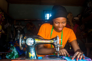 young african woman who is a tailor working on a dress smiling