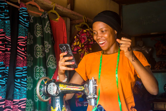 young african woman who is a tailor feeling excited and happy and jubilant while viewing content on her mobile phone