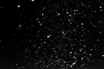 Falling  snow at night. Bokeh lights on black background, flying snowflakes in the air. Overlay texture. Snowstorm