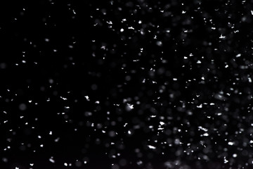 Falling  snow at night. Bokeh lights on black background, flying snowflakes in the air. Overlay texture. Snowstorm