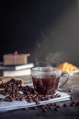 a cup of hot espresso coffee drink with smoke and roasted coffee beans on the table in the morning. vertical image, cropped shot