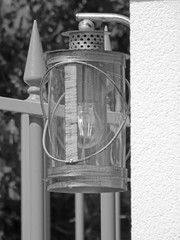 Western styled lamp with clear mainly cylindrical transparency glass parts and modern bulb. Old styled metallic finition on a crepy pillar. Vertical black and white photography