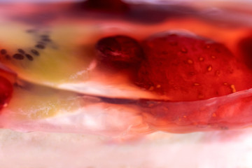 Close-up of blurred strawberries, cherries and kiwi in sweet jelly on pink nougat / background of berries and fruits with soft selective focus