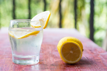 A glass of lemonade and cut lemon on a red table
