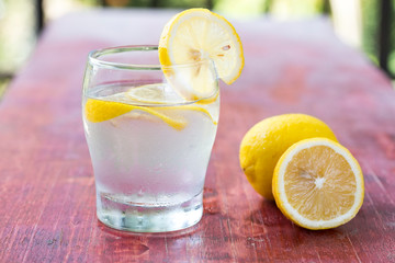 A glass of lemonade and cut lemon on a red table