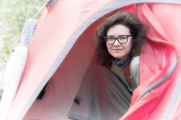 Beautiful young woman in glasses peeks out of a tent in the morning