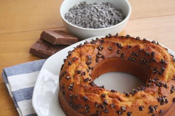 Sweet cake with small pieces of dark chocolate on a plate on wooden table