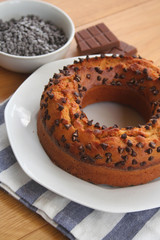Sweet cake with small pieces of dark chocolate on a plate on wooden table