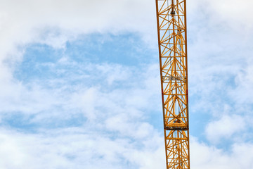 Background with closeup of yellow crane arm against a blue sky with clouds. Seen in on a construction site in Bavaria, Germany in September.