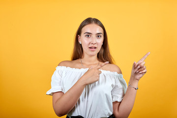 Confused attractive young woman isolated on orange background in studio pointing aside with opened...