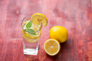 A glass of lemonade and cut lemon on a red table