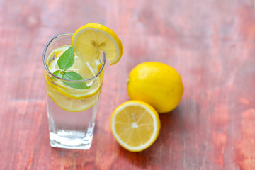 A glass of lemonade and cut lemon on a red table