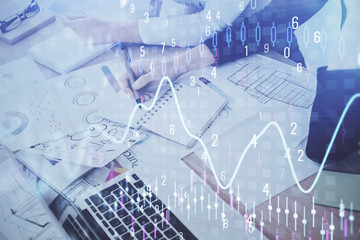 A woman hands writing information about stock market in notepad. Forex chart holograms in front. Concept of research. Double exposure