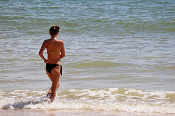 Sea vacations, slim girl in bikini going to swim, rear view. Concept of swimming, sexy body, sunny holidays and enjoying the water