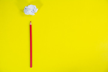 red color wooden pencil with a crushed paper page on yellow background top view