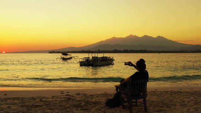 Samar Island, Philippines - Tourist Woman Sitting On the Wooden Chair On the Beach While Watching The Beautiful Sunset - Wide Shot