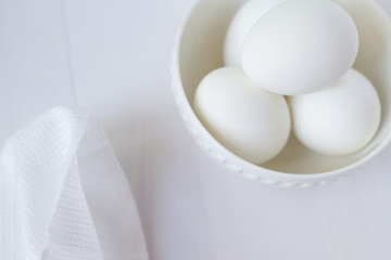four white eggs lie in a plate on a white wooden table next to a towel.