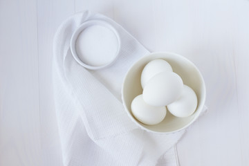 Fototapeta na wymiar four white eggs lie in a plate on a white wooden table next to a towel and salt shaker.