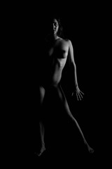 Vertical grayscale shot of an attractive naked female posing for a photoshoot in the darkness
