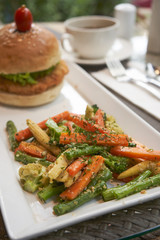 Burger with fried vegetables and coffee at the background on the restaurant table