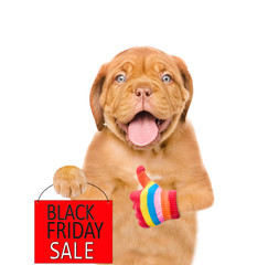 Funny dog holds shopping bag with black friday text and shows thumbs up gesture. isolated on white...