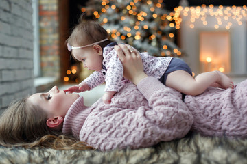 Happy mother with newborn daughter on a background of the Christmas tree. New Year. Christmas and family concept.Portrait of a happy young mother playing with her little daughter in a bright room on C