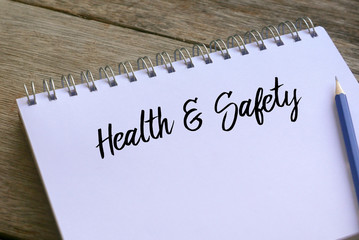 Pencil and notebook written with Health And Safety on wooden background.