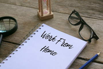 Magnifying glass,sand clock,glasses,pencil and notebook written with Work From Home on wooden background.