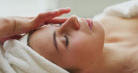 Close up of a beautiful young smiling woman with a towel on her head is receiving a facial massage and spa treatment for perfect skin in a luxury wellness center. - Powered by Adobe