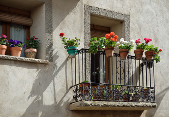 Fototapeta na wymiar There are a row of the flowerpots with flowering plants of pelargonium in the balcony of the Spanish town.