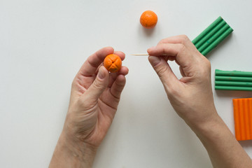 Woman hands showing dot on orange ball made by tooth stick to create orange fruit from polymer clay