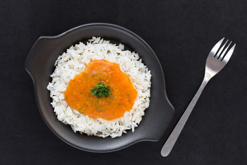 Rice with pumpkin sauce on black plate on black background