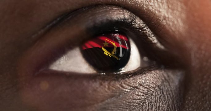 Woman black eye in close up with the flag of Angola in iris with wind motion. video concept