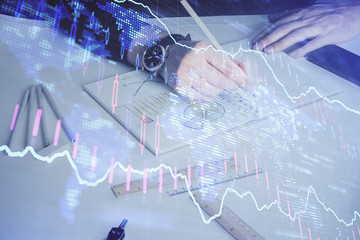 Double exposure of man's hands writing notes of stock market with forex chart.