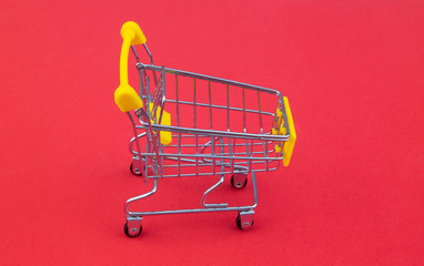 Yellow shopping cart or trolley on red background close up