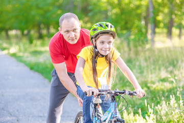 Obraz premium Father helps daughter learn to ride a bike in summer park