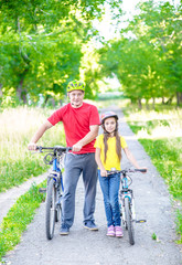 Portrait of the father and his little daughter with bikes stand in the summer park together
