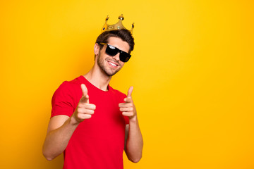Portrait of cheerful cool guy have gold diadem point index finger in camera choose best team ever wear red t-shirt isolated over bright color background