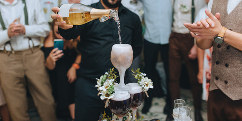 The bartender, man pours champagne and alcohol into a glass that foams at the party. Beautiful decoration of wineglasses with flowers. To celebrate a successful deal.