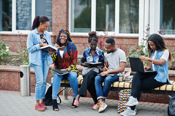 Fototapeta premium Group of five african college students spending time together on campus at university yard. Black afro friends studying at bench with school items, laptops notebooks.